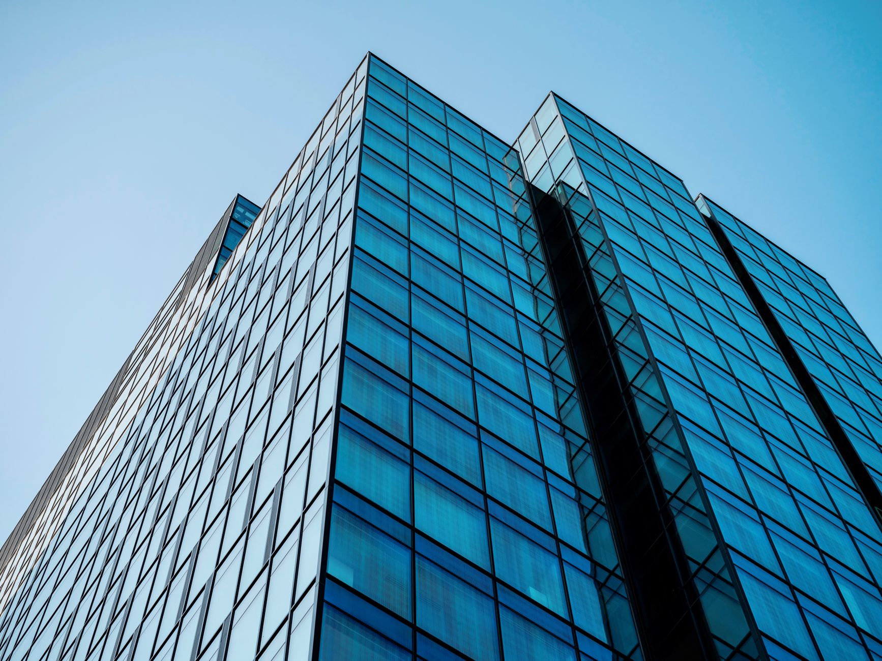 Façade vitrée d’un immeuble de bureaux vue d’en bas, sous un ciel bleu clair