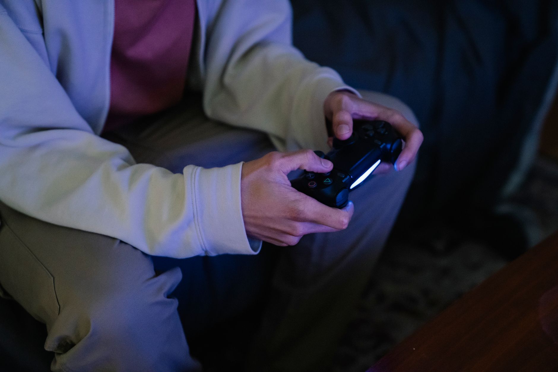 Gros plan sur les mains d’une personne tenant une manette de jeu vidéo noire allumée.