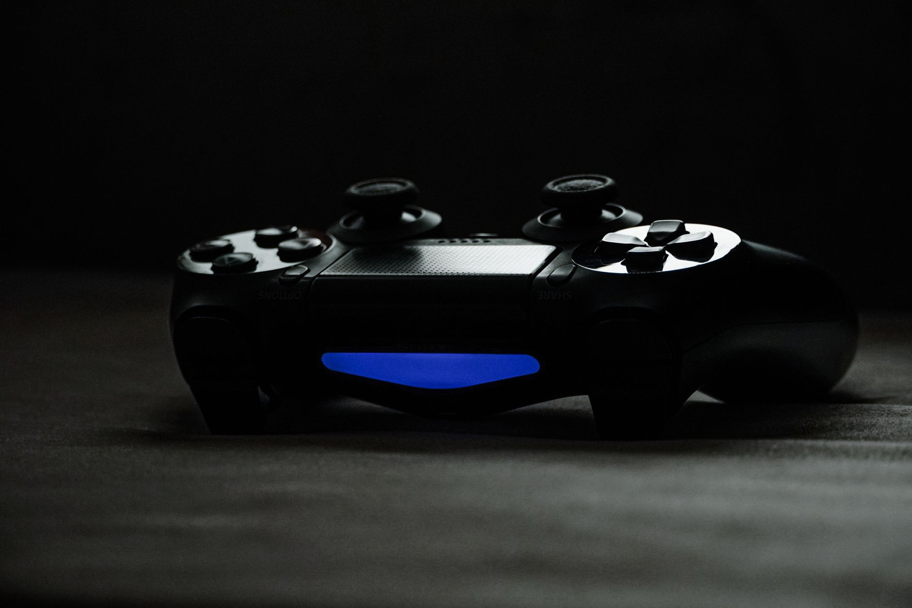 Manette de jeu noire posée dans la pénombre, avec une barre lumineuse bleue allumée sur sa face avant.